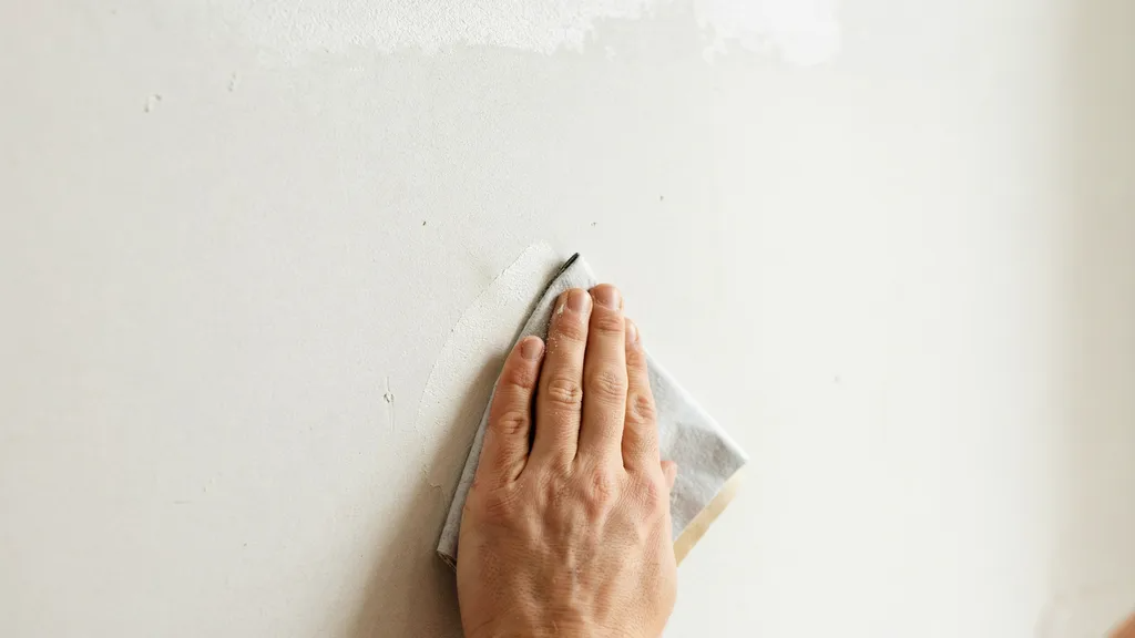 Person sanding a primed wall to improve paint adhesion.