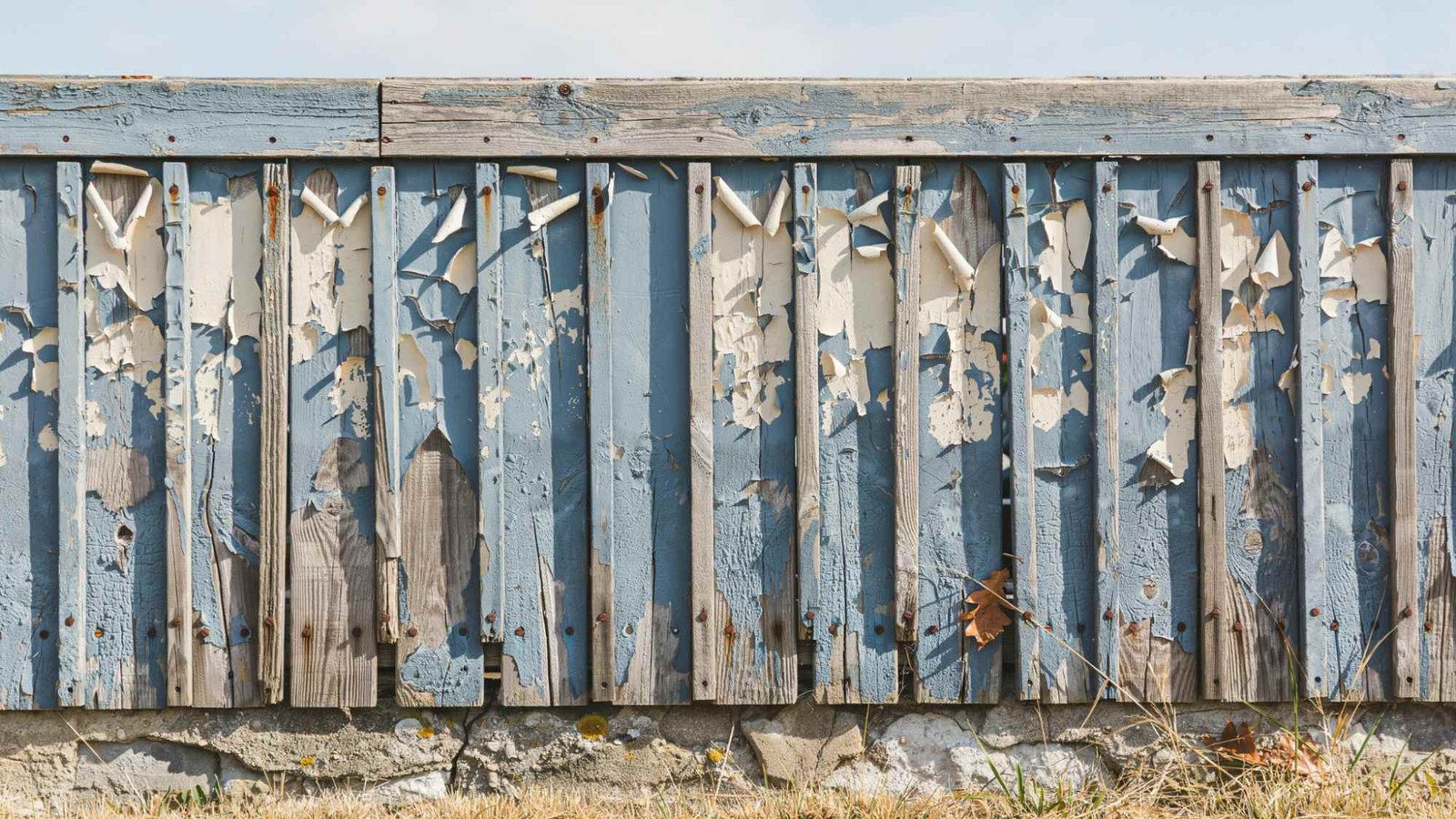 Outdoor surface with peeling flaking paint and uneven finish revealing damage caused by using interior paint outside over time.
