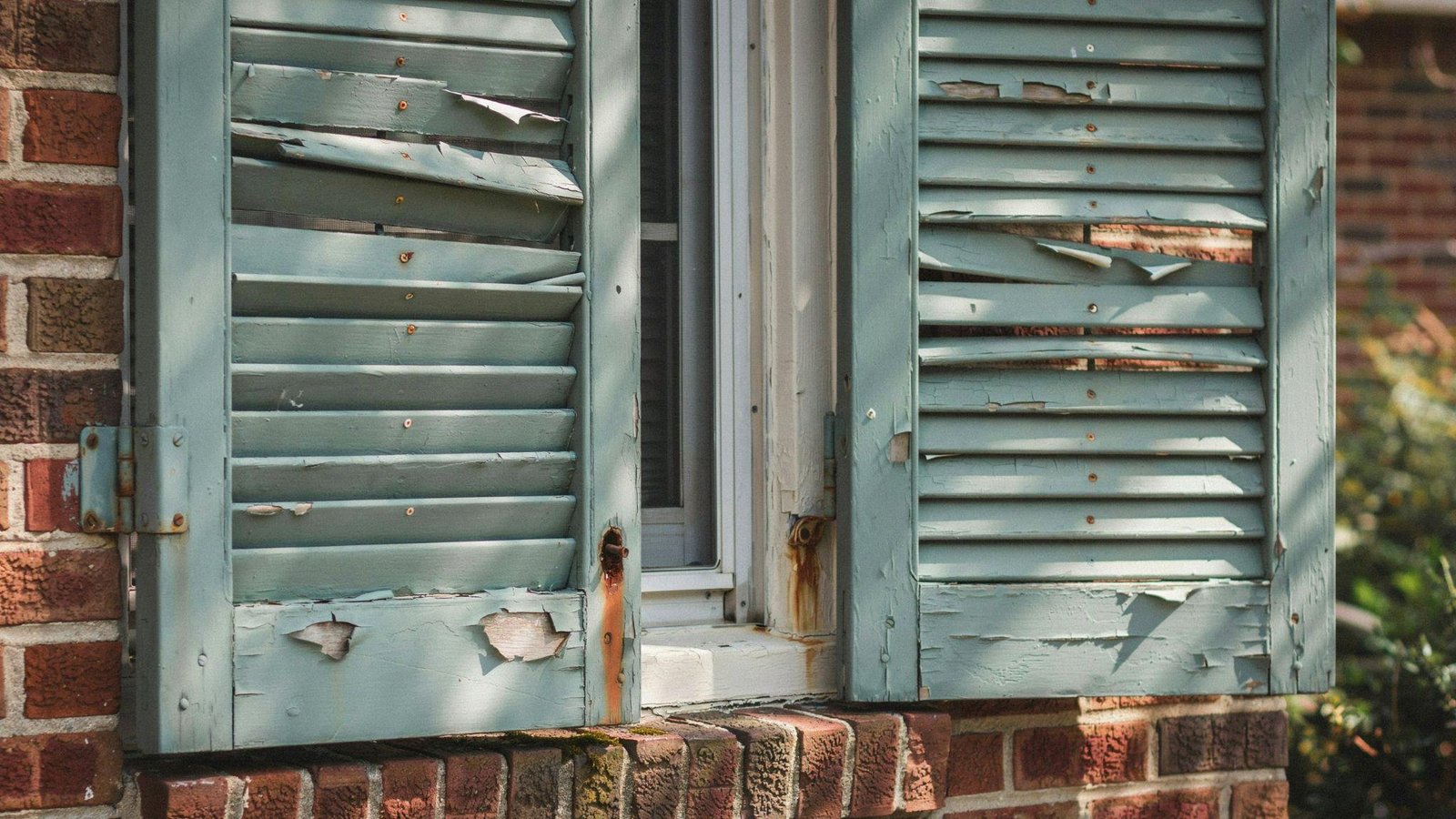 Weathered house shutters with cracked paint, minor wood damage, and loose hardware before repainting.