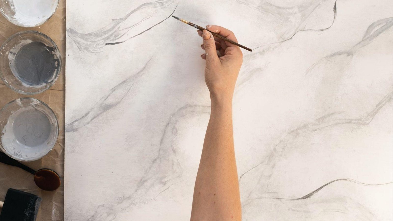 Hand paints gray marble veining on white surface using fine brush, faux marbling technique demo