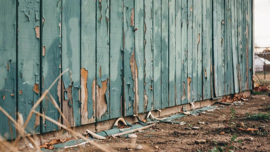 Peeling paint chips from outdoor surface falling onto ground showing environmental damage and surface deterioration due to incorrect paint usage.