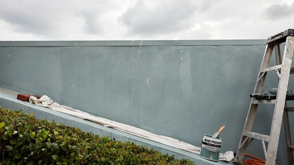Freshly painted exterior wall exposed to light rain with droplets forming and cloudy outdoor weather conditions visible.