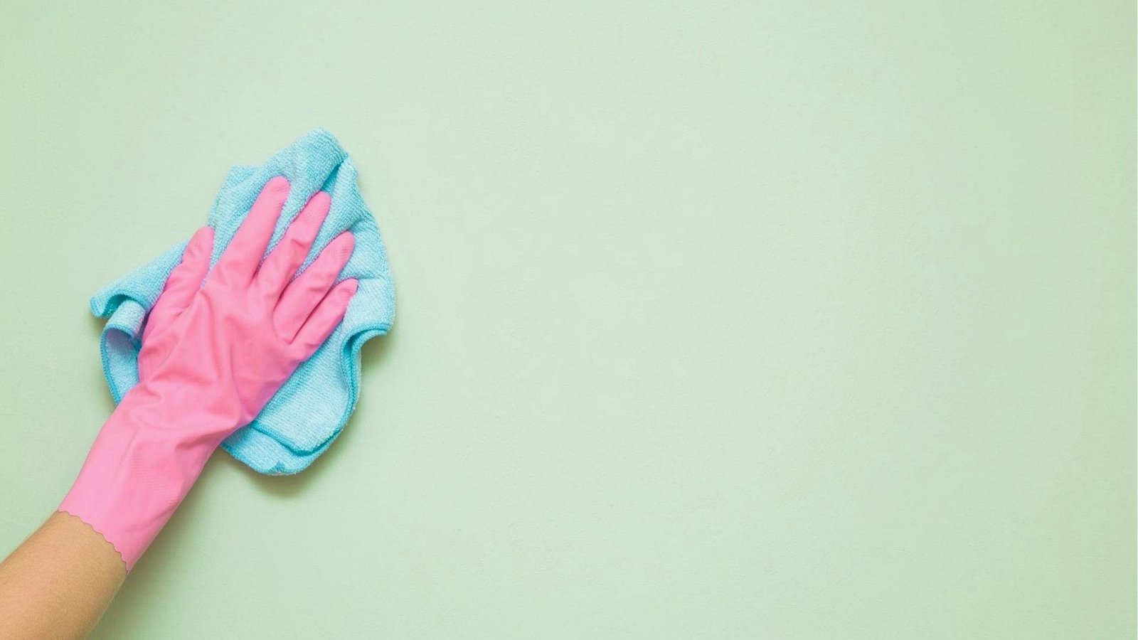 Hand in pink rubber glove wiping a light green painted wall with a blue microfiber cloth.