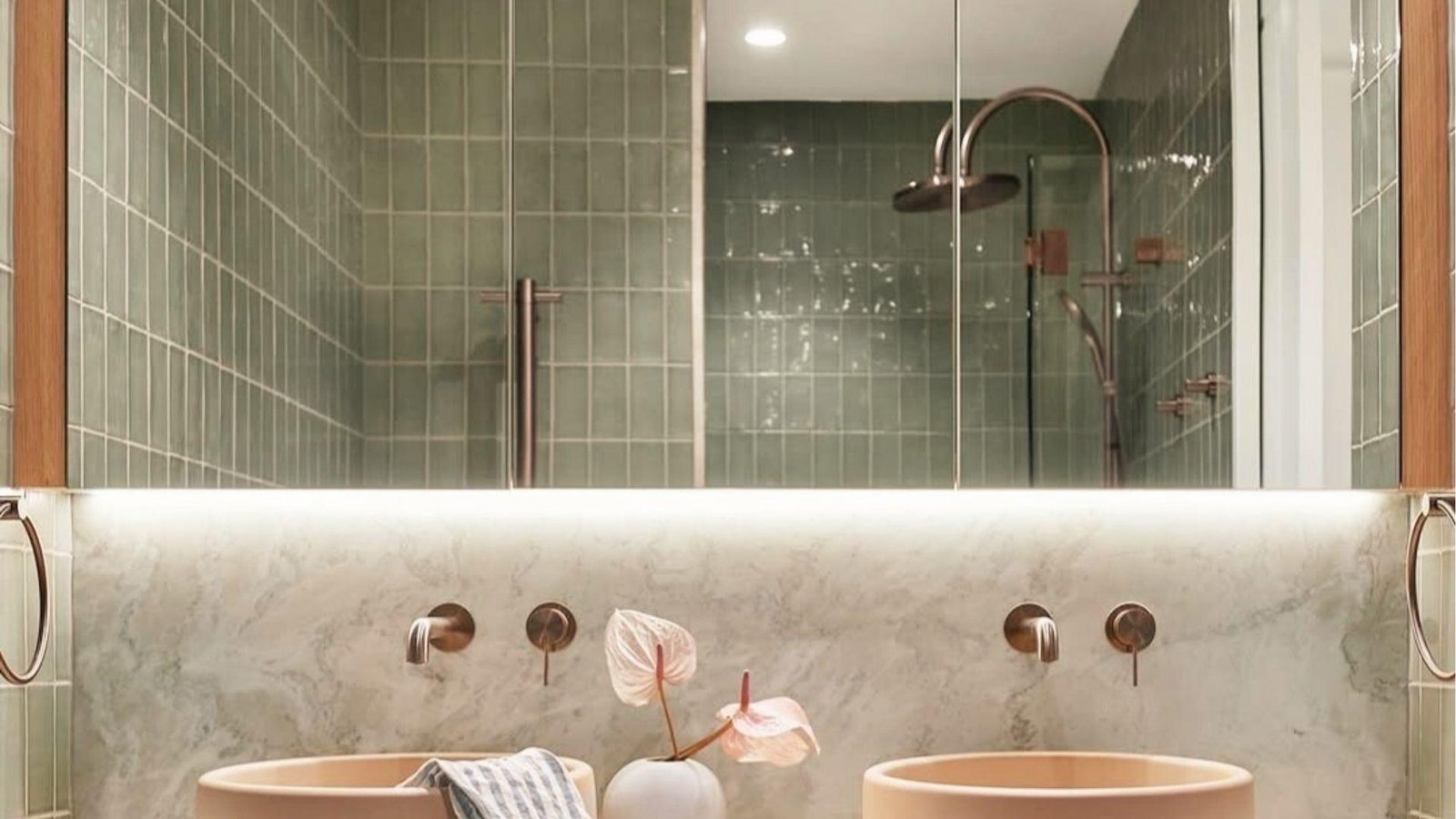 Minimal sage green tiled bath with dual peach sinks, marble backsplash, and brushed gold taps.