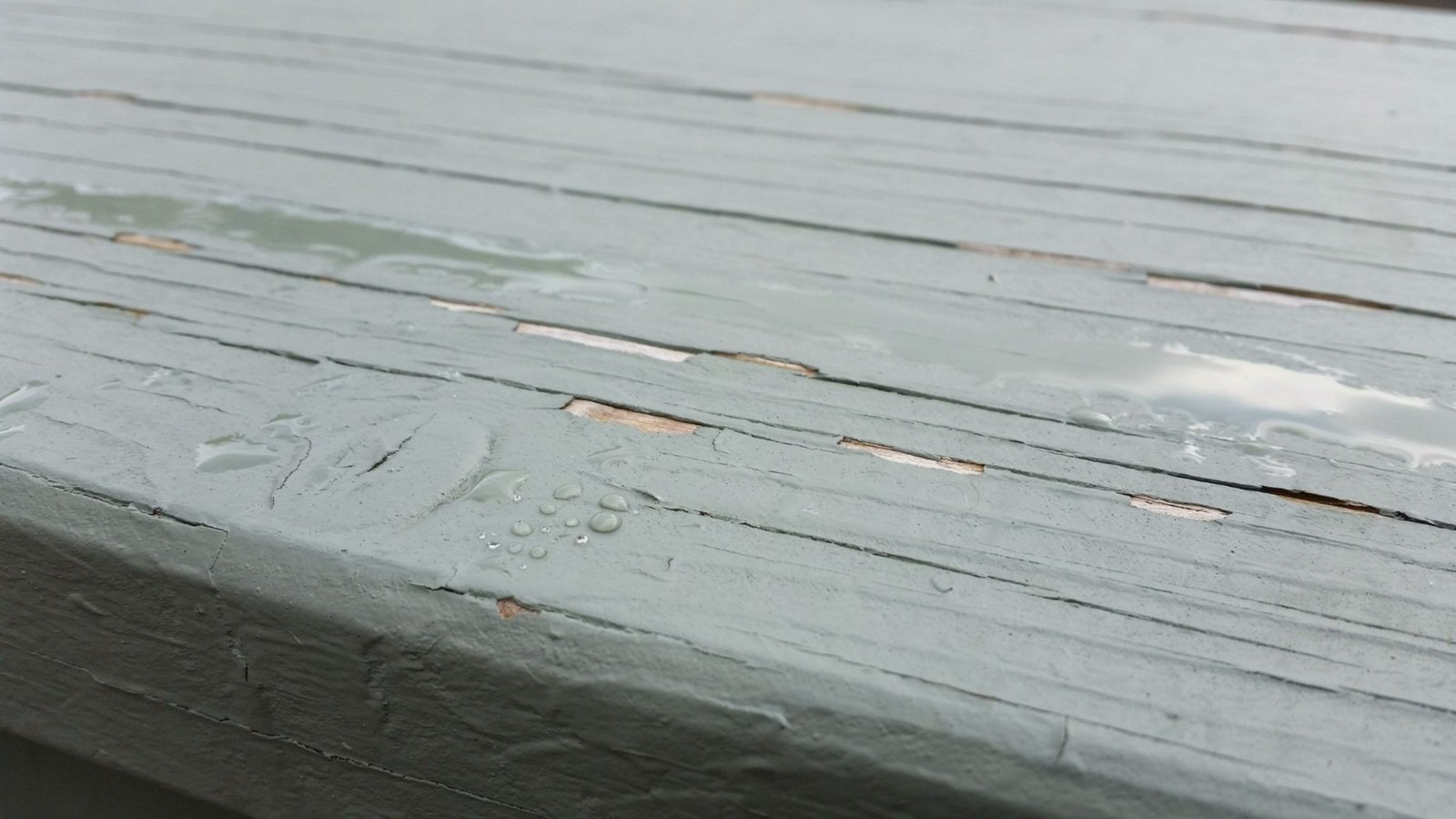 Outdoor painted surface coated with clear sealant showing slight gloss but underlying paint still deteriorating under weather exposure conditions.