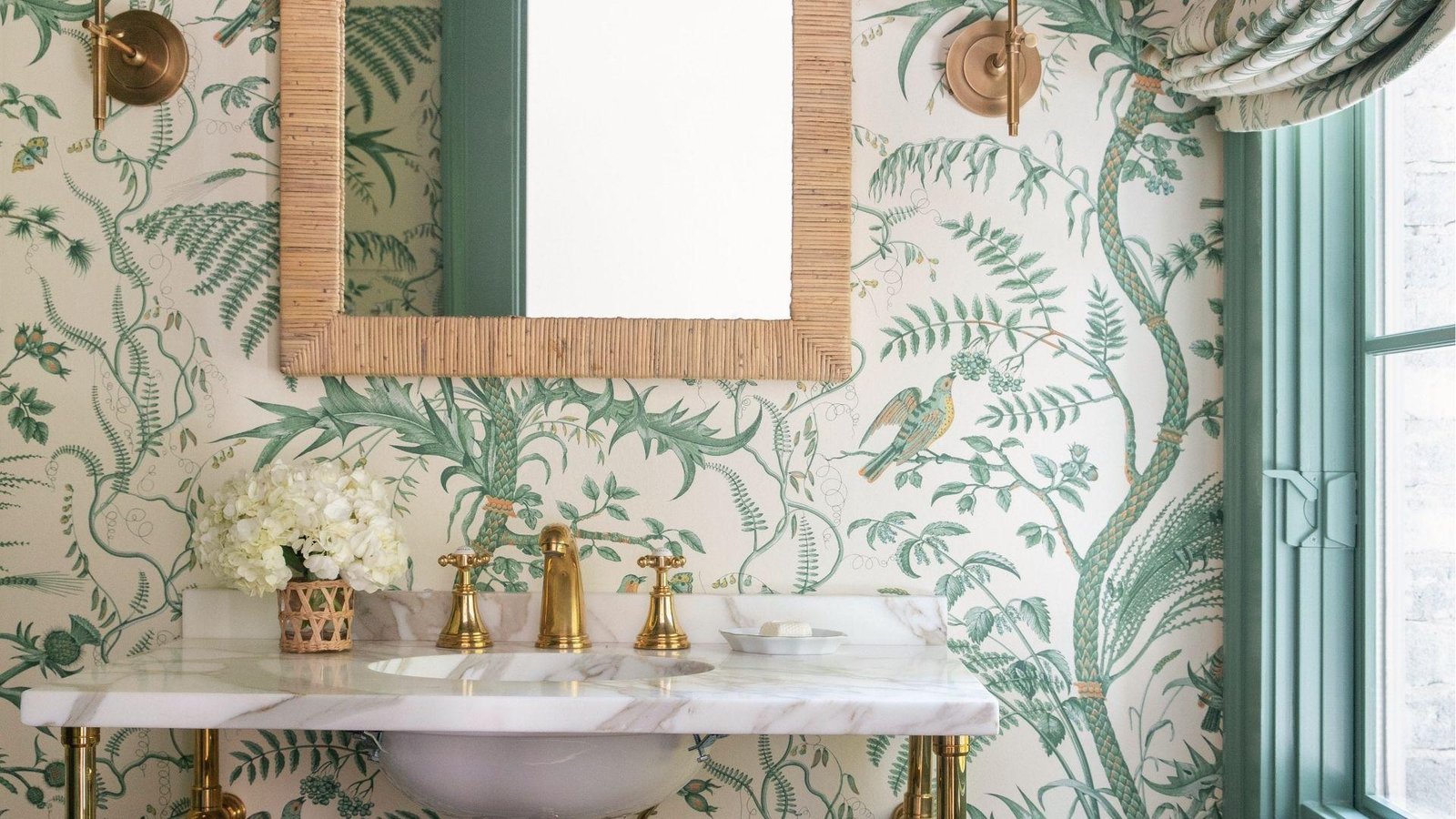 Botanical powder room with green leaf wallpaper, rattan mirror, marble vanity, and gold hardware.