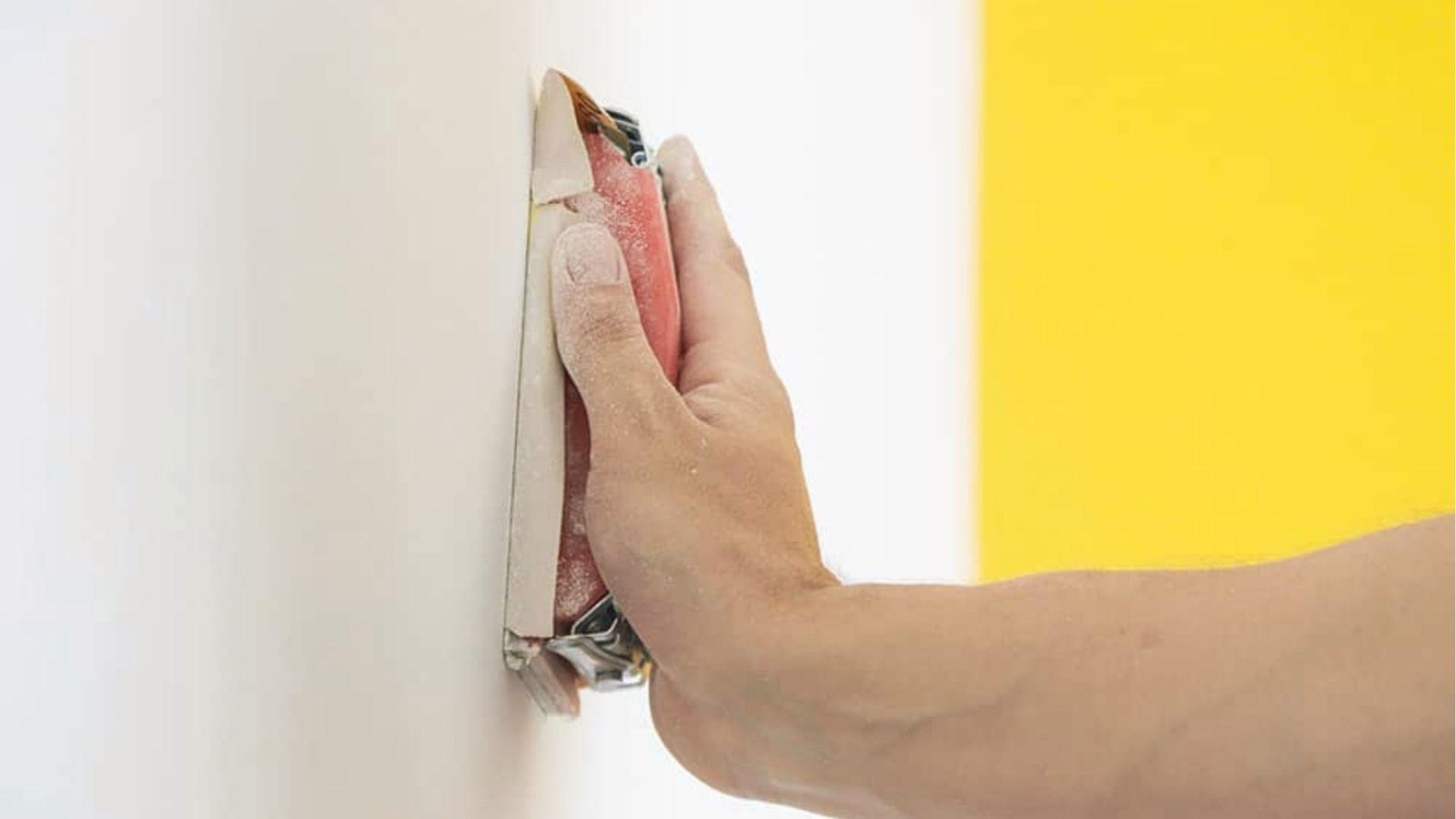 Hand sands white wall prep next to yellow section, surface smoothing for faux paint application