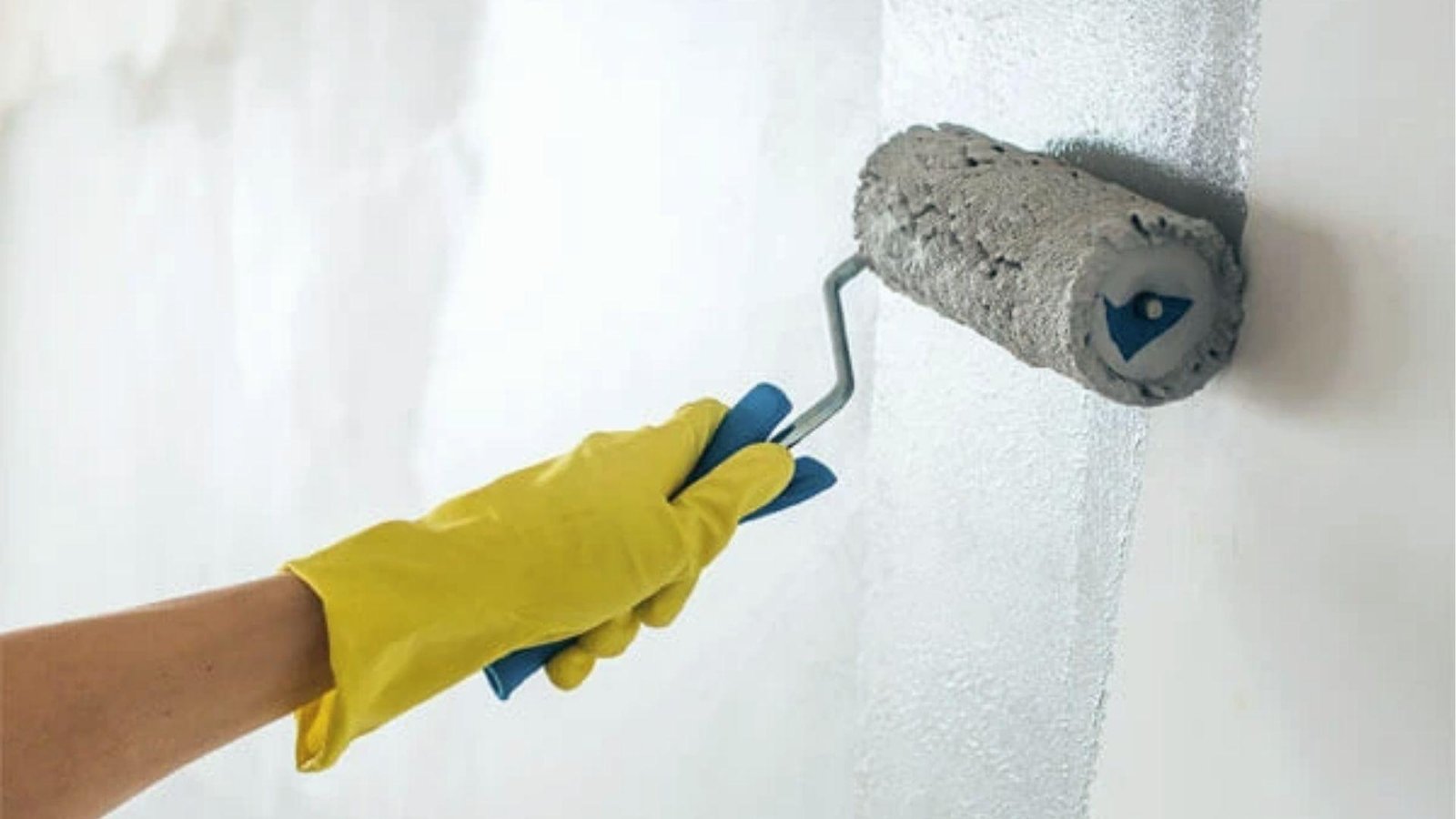 Gloved hand rolls elastomeric paint on white wall, a key advantage is superior crack bridging.