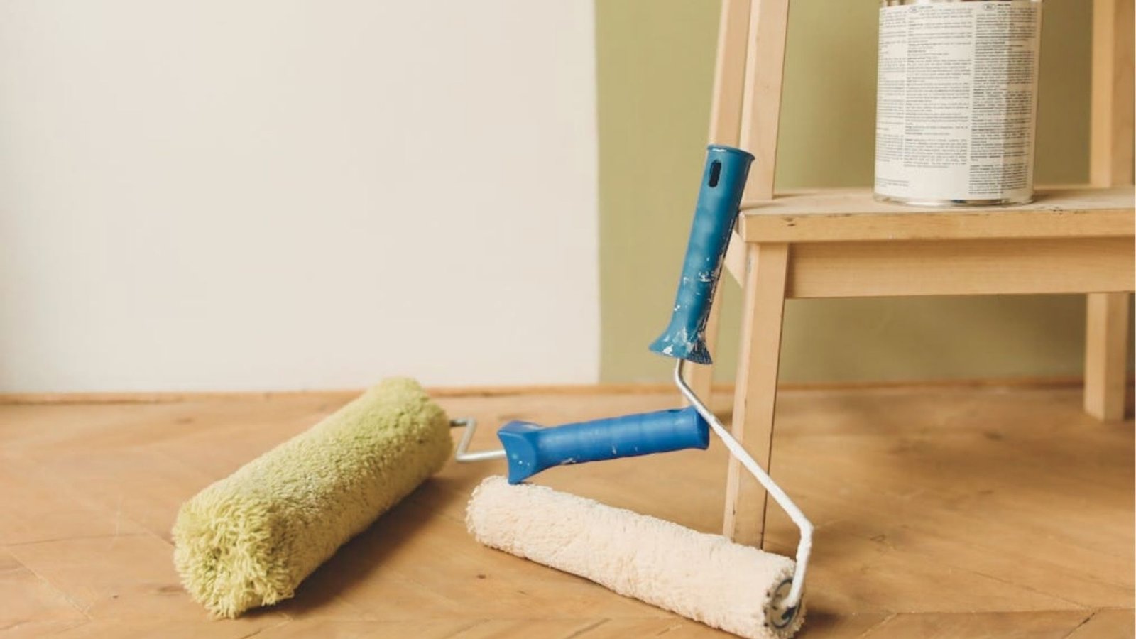 A paint roller and a can of paint resting on a wooden floor, ready for a painting project.